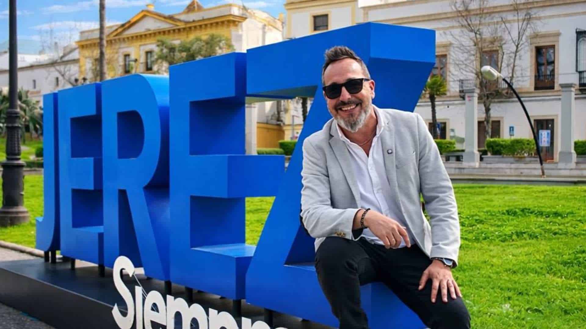 Luis Pereira, conocido como el influencer Mister Fog Jerez, sonriendo y posando junto a las letras azules gigantes de 'JEREZ' en la Plaza de la Asunción, promocionando el turismo de la ciudad para VeoAndalucía.