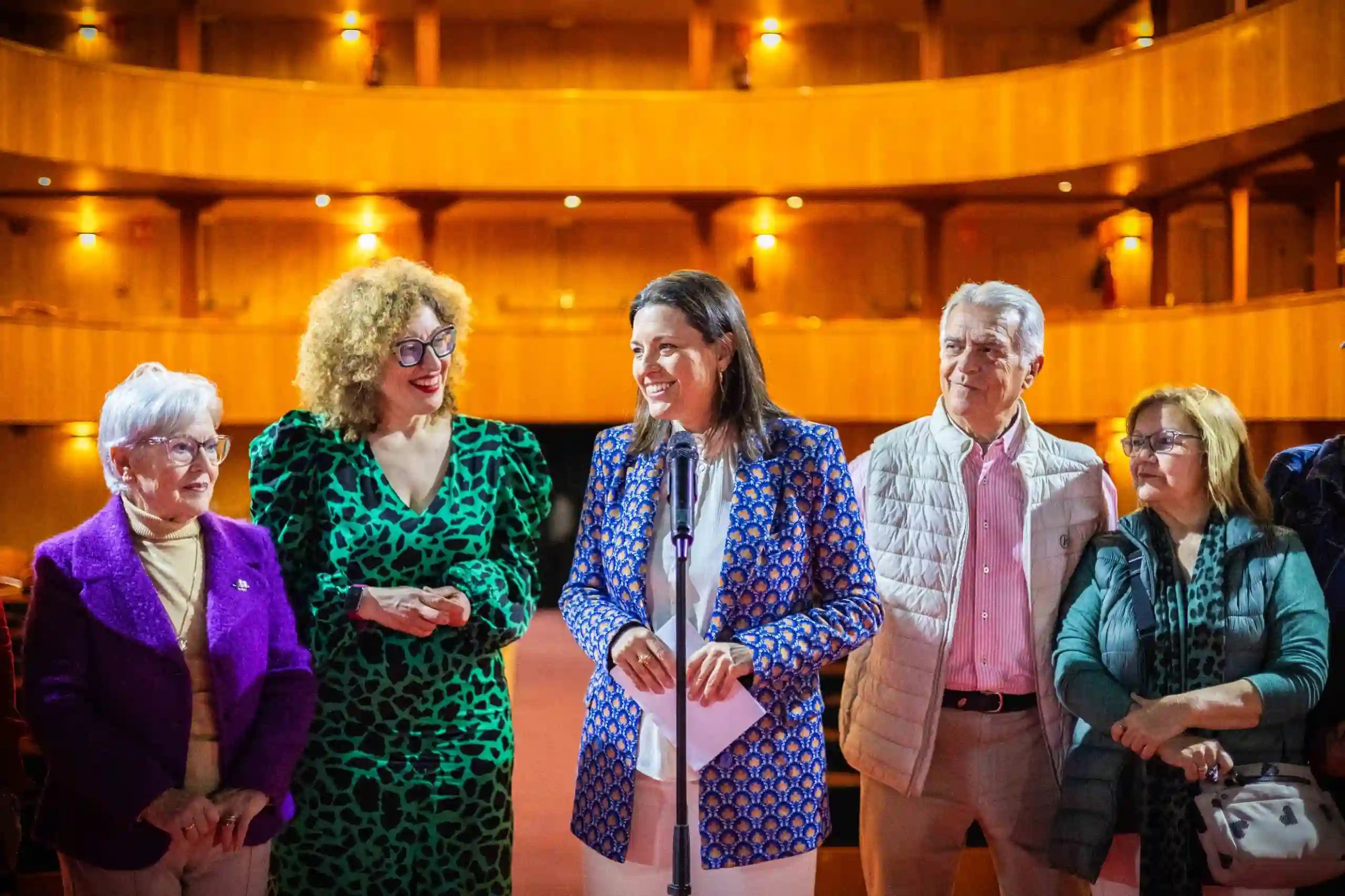 La Alcaldesa de San Fernando, Patricia Cavada, y 5 personas más posan en el interior de un teatro iluminado; una mujer en el centro habla al micrófono durante un acto oficial.