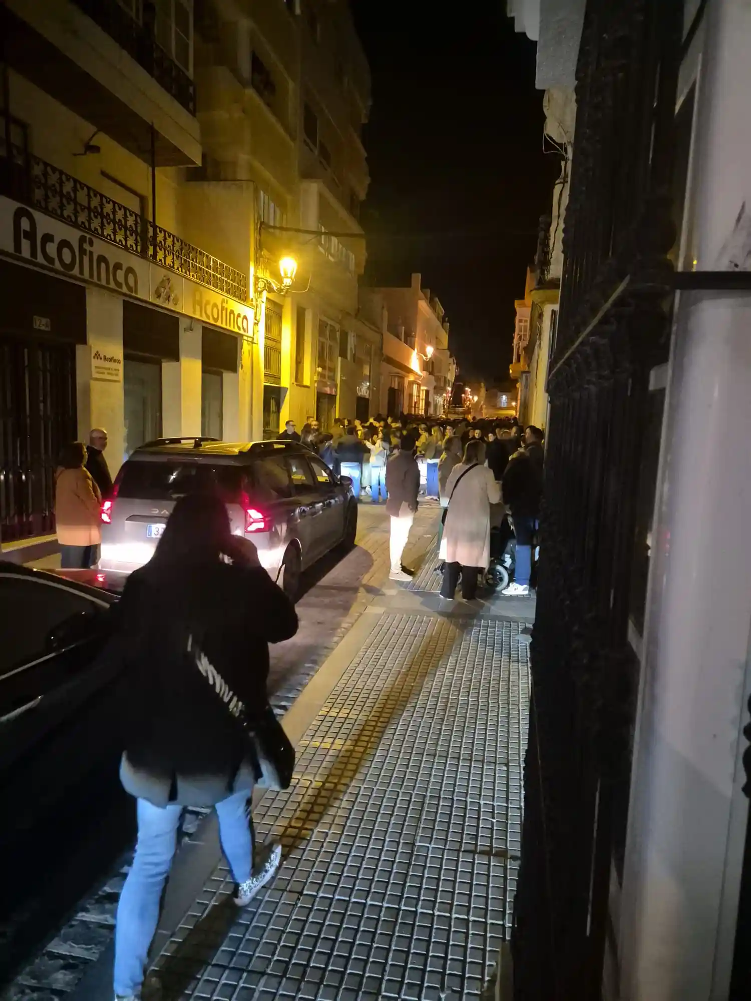 Nazareno avanzando por la calle Pérez Galdós de San Fernando mientras varios vehículos esperan durante la noche.