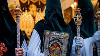 Tres nazarenos de la Hermandad de la Esperanza de Huelva con túnica blanca y antifaz de terciopelo verde, el central portando el Libro de Reglas.