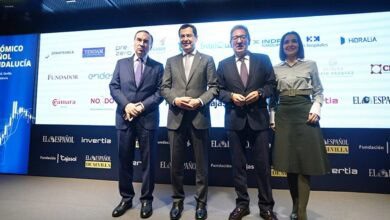 Imagen de cuatro personas en un acto oficial con fondo de patrocinadores y logotipos.