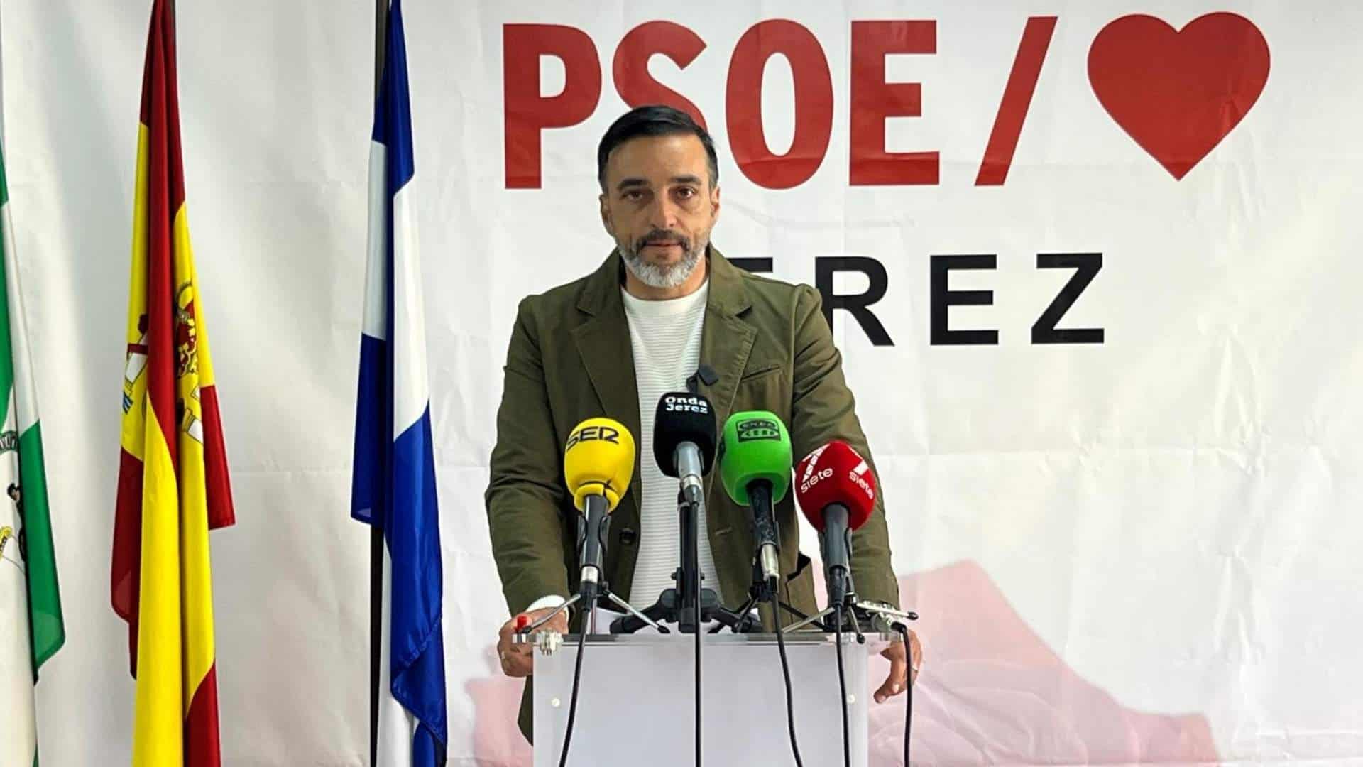 El portavoz del PSOE en Jerez durante una rueda de prensa con banderas y micrófonos.