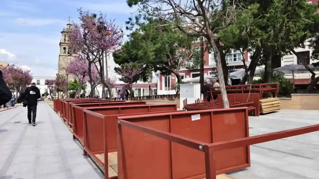 Estructuras de los palcos de Semana Santa instaladas en una plaza de Sanlúcar de Barrameda con la torre de la Parroquia de la O al fondo.