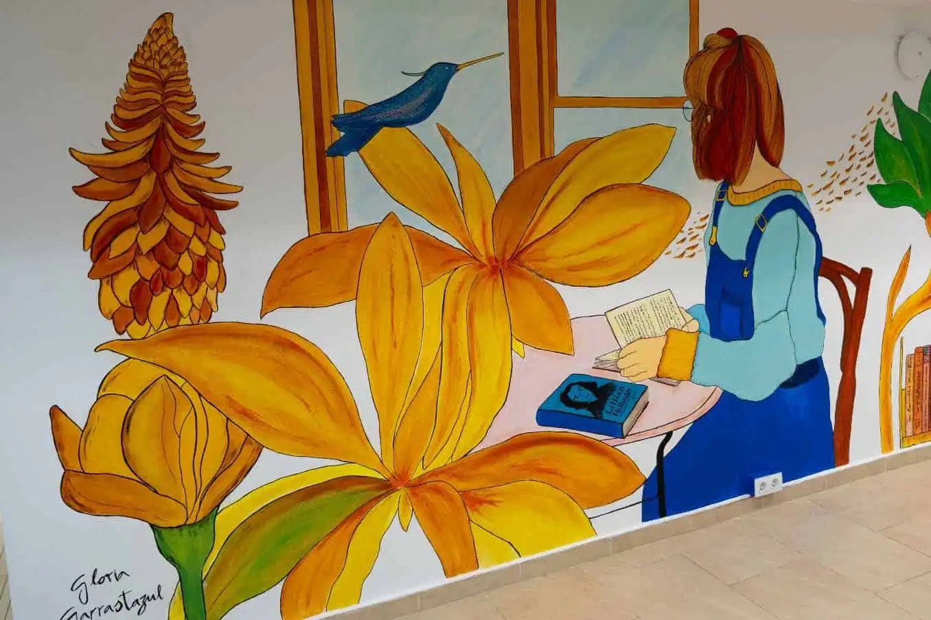 Mural en la biblioteca Santa María con flores y una niña leyendo, obra de Gloria Garrastazul.