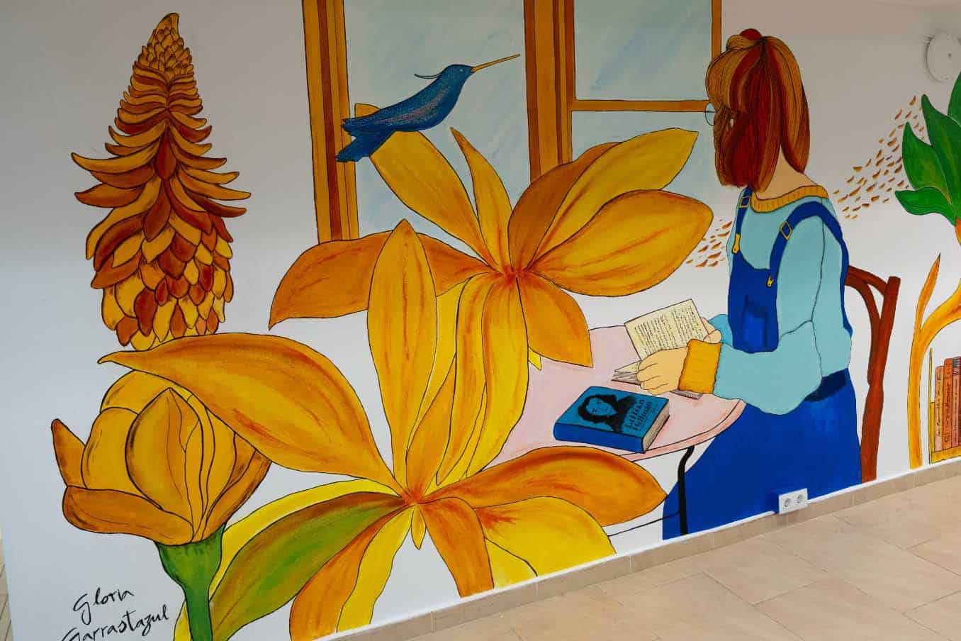 Mural en la biblioteca Santa María con flores y una niña leyendo, obra de Gloria Garrastazul.
