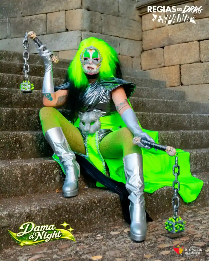 Dama D’night representa a San Fernando en el reality show “Regias del Drag España”, con maquillaje artístico y fondo vibrante.