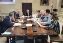 Reunión de la Junta de Gobierno Local de Sevilla presidida por el alcalde en una mesa de madera con documentos y micrófonos.