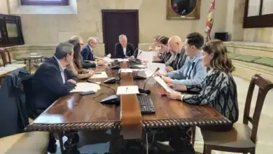 Reunión de la Junta de Gobierno Local de Sevilla presidida por el alcalde en una mesa de madera con documentos y micrófonos.