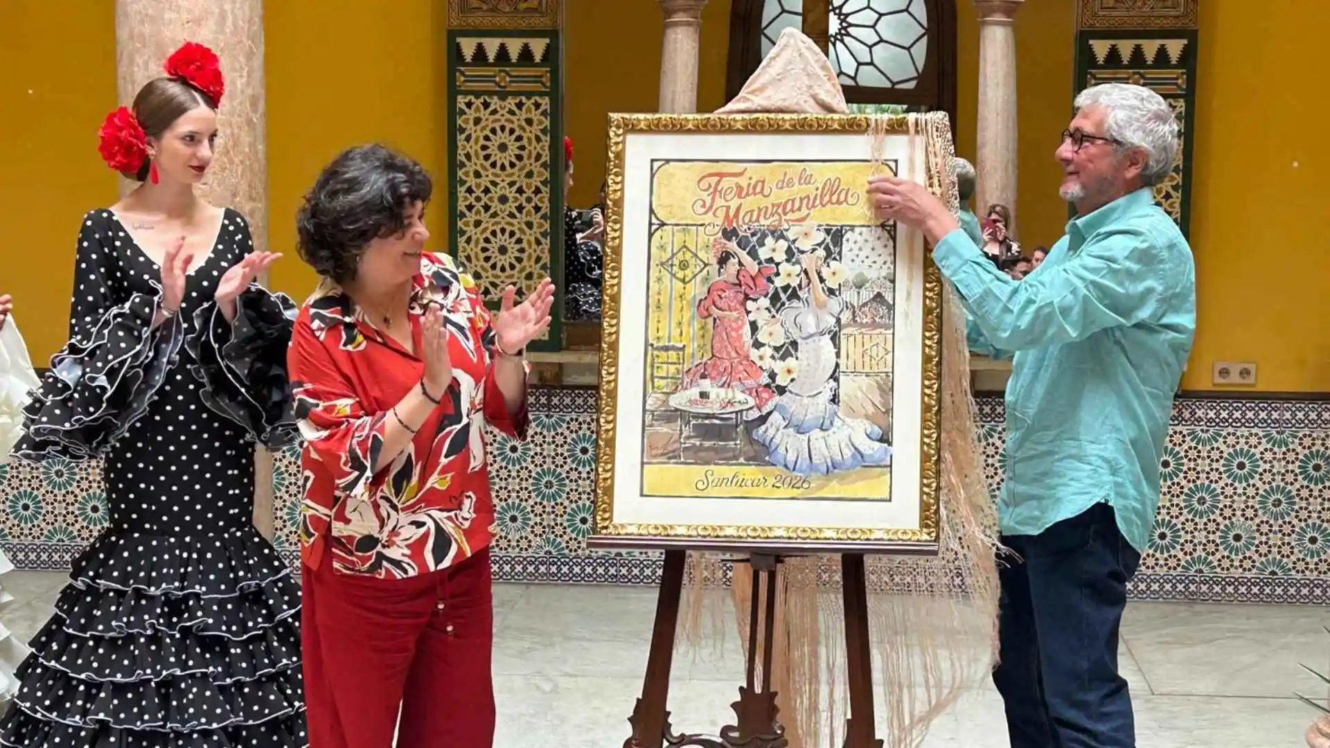 La alcaldesa Carmen Álvarez y el artista José Antonio Ramírez Harana descubren el cartel de la Feria de la Manzanilla 2026 en Sanlúcar.