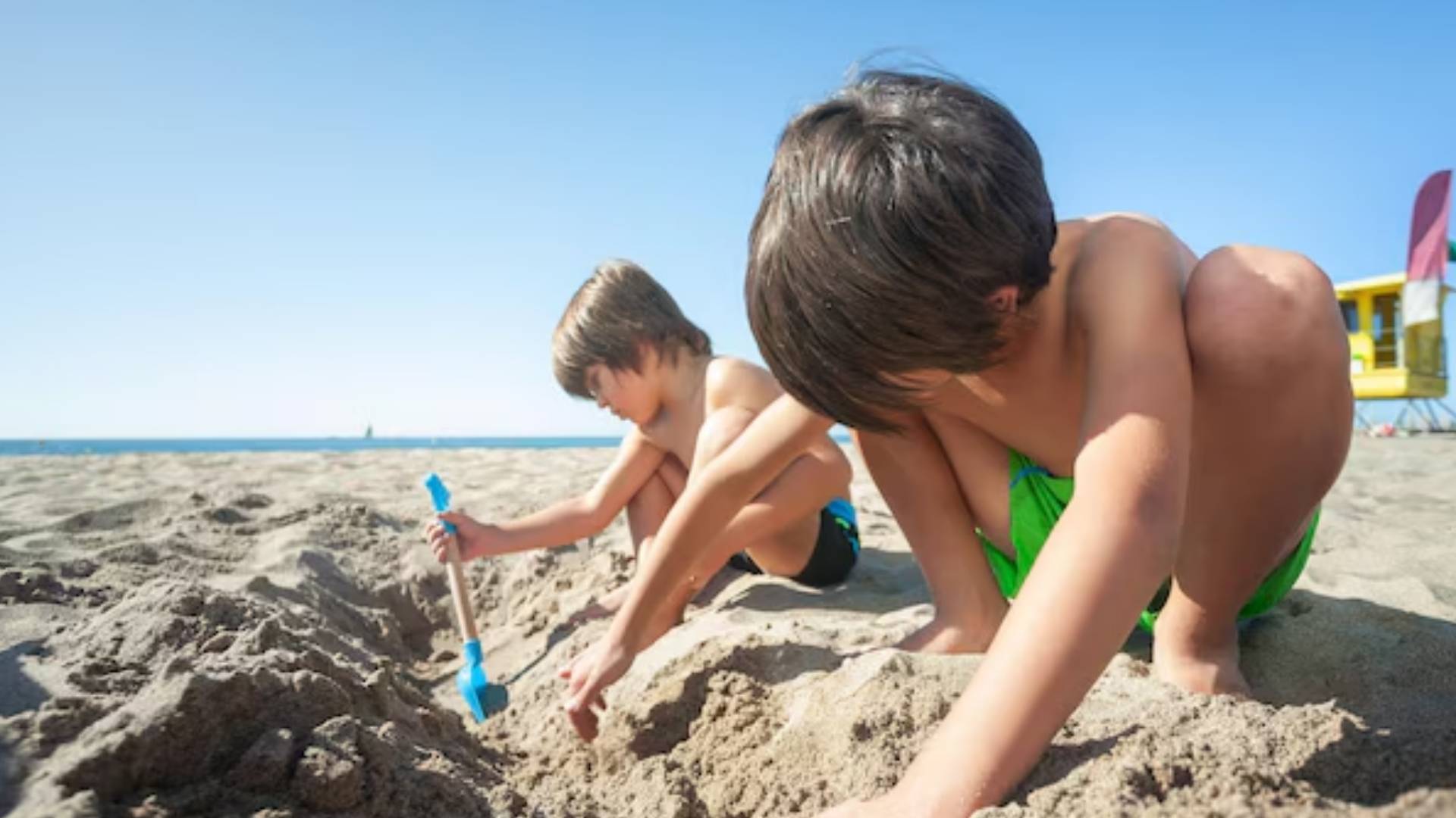 Niños jugando a excavar arena en la playa, actividad que puede conllevar multas de hasta 200.000 euros según la Ley de Costas.