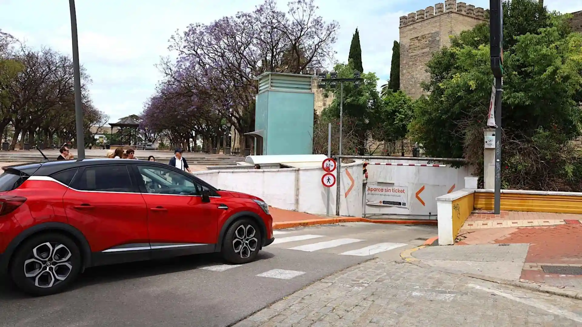 Coche eléctrico rojo circulando junto a la entrada del aparcamiento de la Alameda Vieja en Jerez, donde se ofrecen puntos de recarga gratuita Telpark.