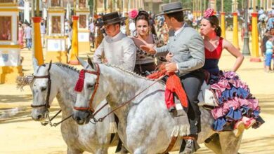 Caballistas y mujeres vestidas de flamenca paseando a caballo por el Real de la Feria del Caballo de Jerez.