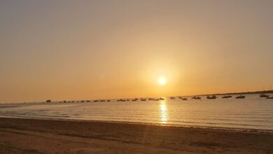 Pueblos con las mejores vistas panorámicas: Puesta de sol dorada en la playa de Sanlúcar de Barrameda con barcos en el mar.