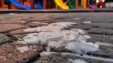 Restos de cera blanca derretida sobre el suelo de un parque infantil con columpios de colores al fondo.