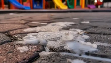 Restos de cera blanca derretida sobre el suelo de un parque infantil con columpios de colores al fondo.
