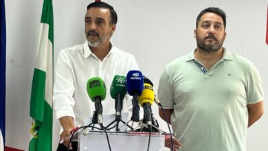 Dos hombres en una rueda de prensa con banderas de Andalucía y España.