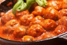 Albóndigas de carne caseras en salsa de tomate tradicional cocinando en una sartén de hierro fundido con albahaca fresca.