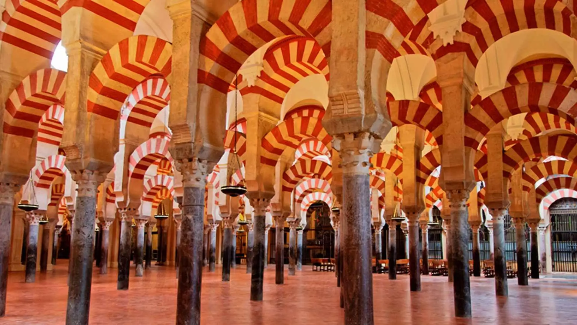 Columnas y arcos de herradura bicolores en rojo y blanco dentro de la Mezquita de Córdoba, reflejo de la herencia árabe y romana.