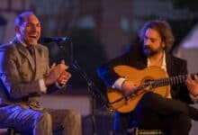 Cantante de flamenco cantando al micrófono junto a un guitarrista tocando la guitarra española en un concierto al aire libre en Andalucía.