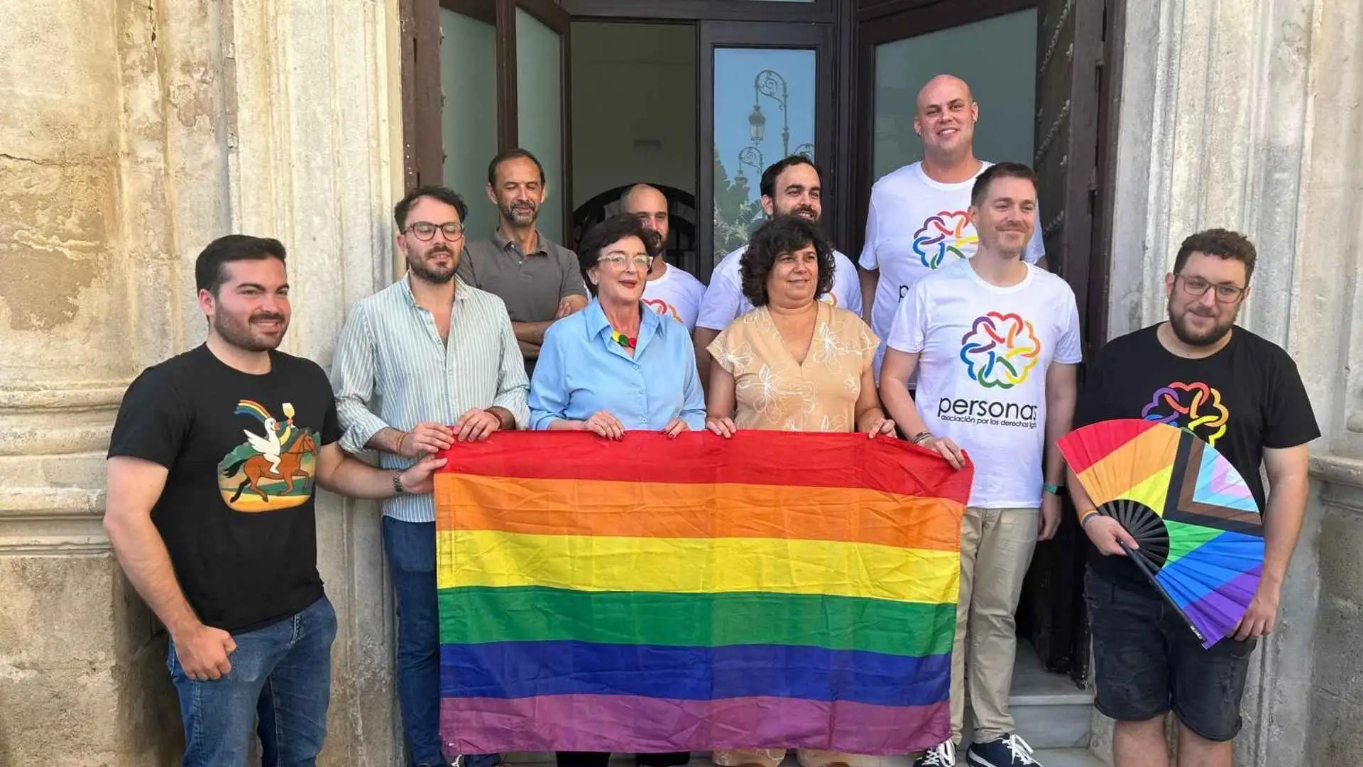 Integrantes de la asociación "personas" sosteniendo una bandera LGTBI+ en un evento conmemorativo.