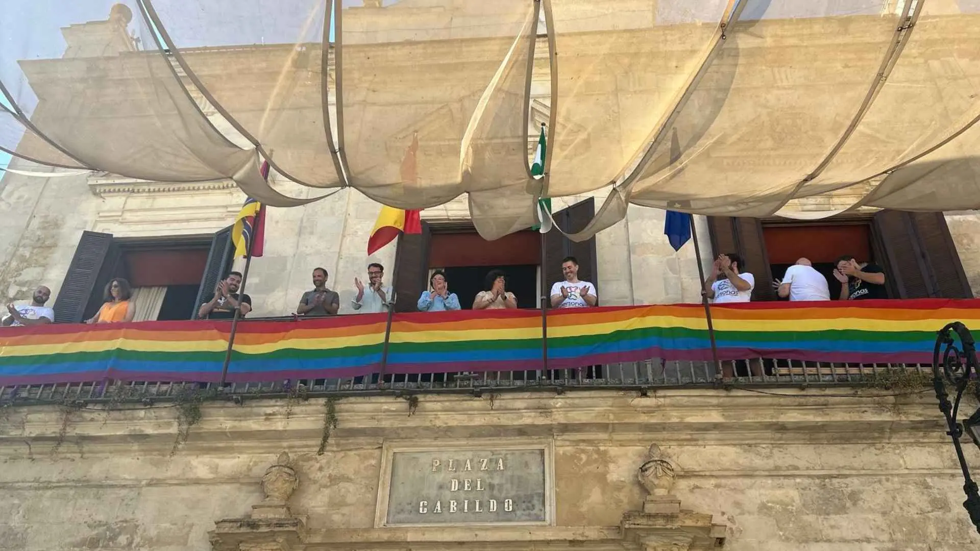 Bandera LGTBI+ desplegada en el balcón de la Plaza del Cabildo durante un acto institucional.