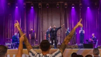 Concierto en vivo con músicos y cantante en escenario iluminado en tonos morados.