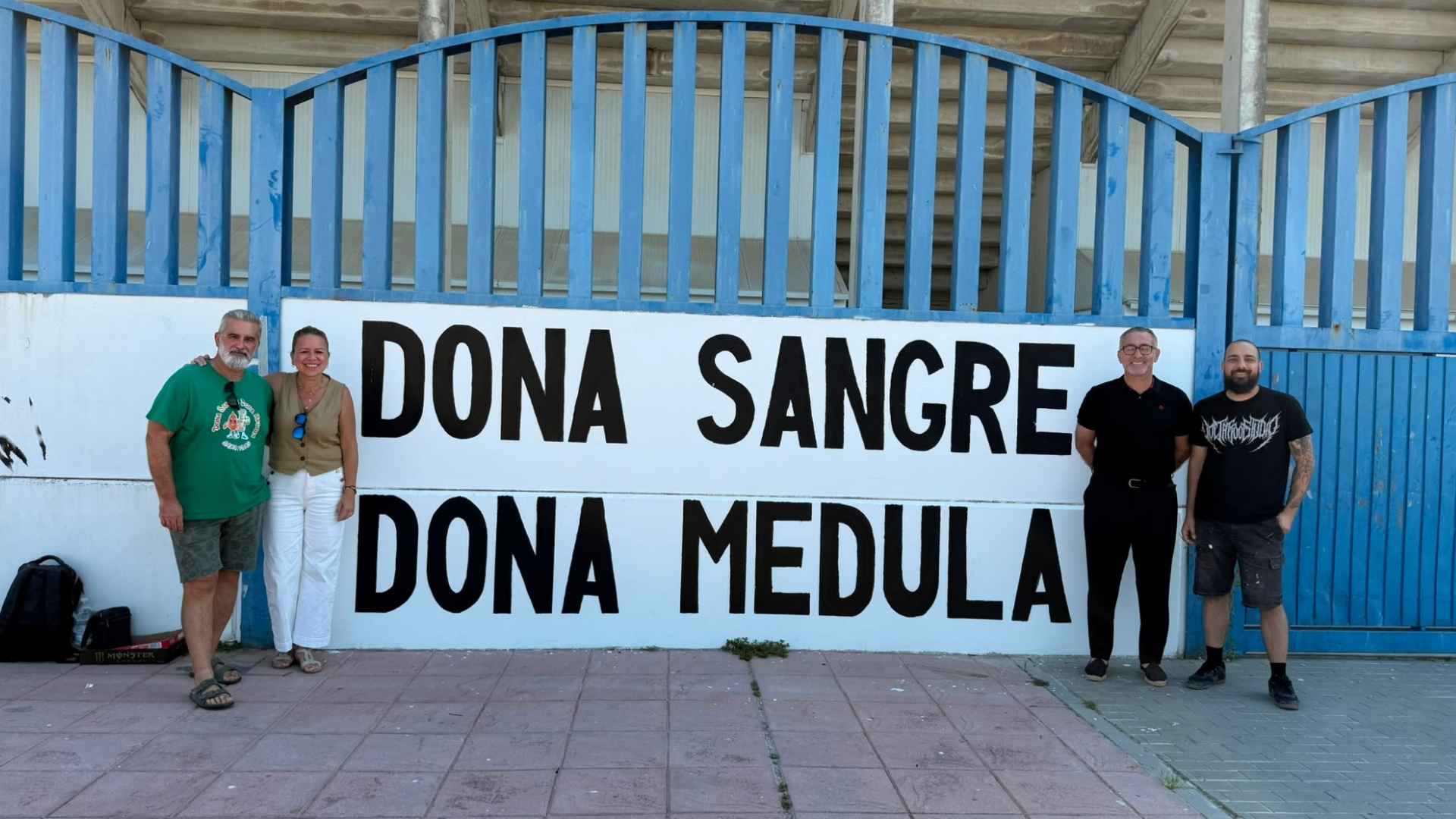 Representantes municipales y miembros de la asociación ApoLeu junto al mural de concienciación sobre la donación de sangre y médula en el Estadio Pedro S. Garrido de Jerez.