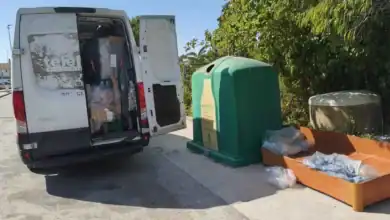 Operarios retirando muebles y residuos abandonados junto a un contenedor de vidrio en la vía pública.