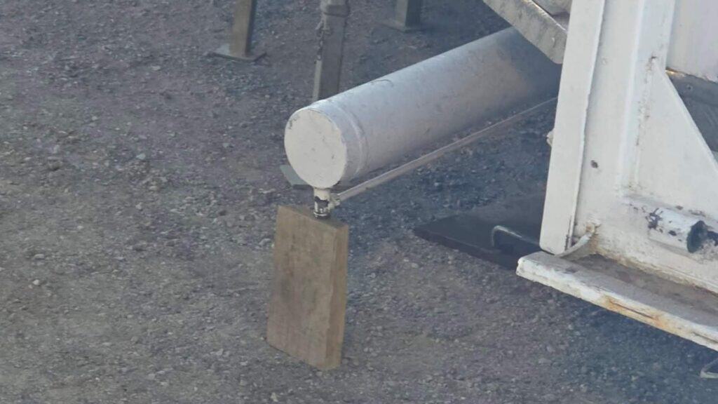 Estructura metálica de una atracción de feria apoyada sobre bloques de madera sobre un suelo de grava.