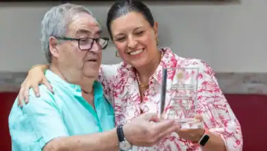 Mujer entregando una insignia de oro a un hombre mayor en un evento.