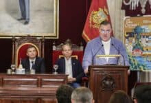 Autoridad en Cádiz hablando en un acto oficial con asistentes en el fondo.