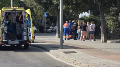 Propuesta visual de una motocicleta de 125cc caída junto a una rotonda urbana de Jerez con una ambulancia y agentes de tráfico al fondo