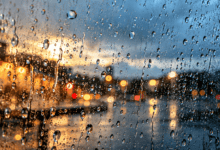 Macrofotografía de gotas de lluvia sobre un cristal con un termómetro exterior desenfocado al fondo
