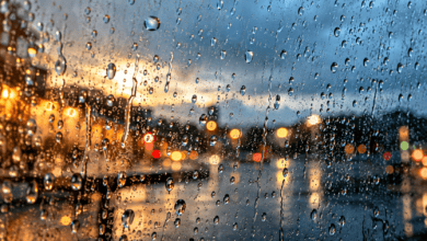Macrofotografía de gotas de lluvia sobre un cristal con un termómetro exterior desenfocado al fondo