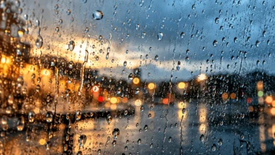 Macrofotografía de gotas de lluvia sobre un cristal con un termómetro exterior desenfocado al fondo