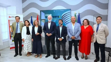 Un grupo de ocho personas, entre hombres y mujeres, posando formalmente frente a una pantalla y banderas institucionales en un acto relacionado con Expoconstruye en Andalucía.