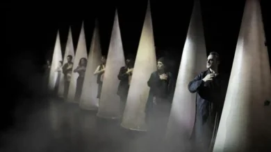 Varios intérpretes vestidos de oscuro aparecen entre estructuras cónicas iluminadas sobre un escenario con humo