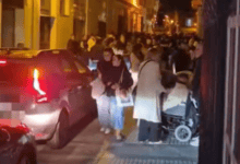 Multitud de personas en la calle de San Fernando durante la noche de Semana Santa con vehículos por medio.