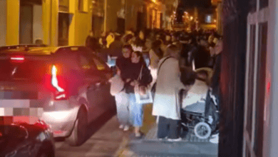 Multitud de personas en la calle de San Fernando durante la noche de Semana Santa con vehículos por medio.