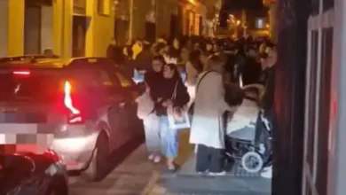 Multitud de personas en la calle de San Fernando durante la noche de Semana Santa con vehículos por medio.