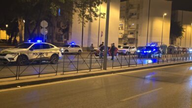 Vehículos policiales con luces azules encendidas y agentes junto a una mediana en una avenida durante la noche.