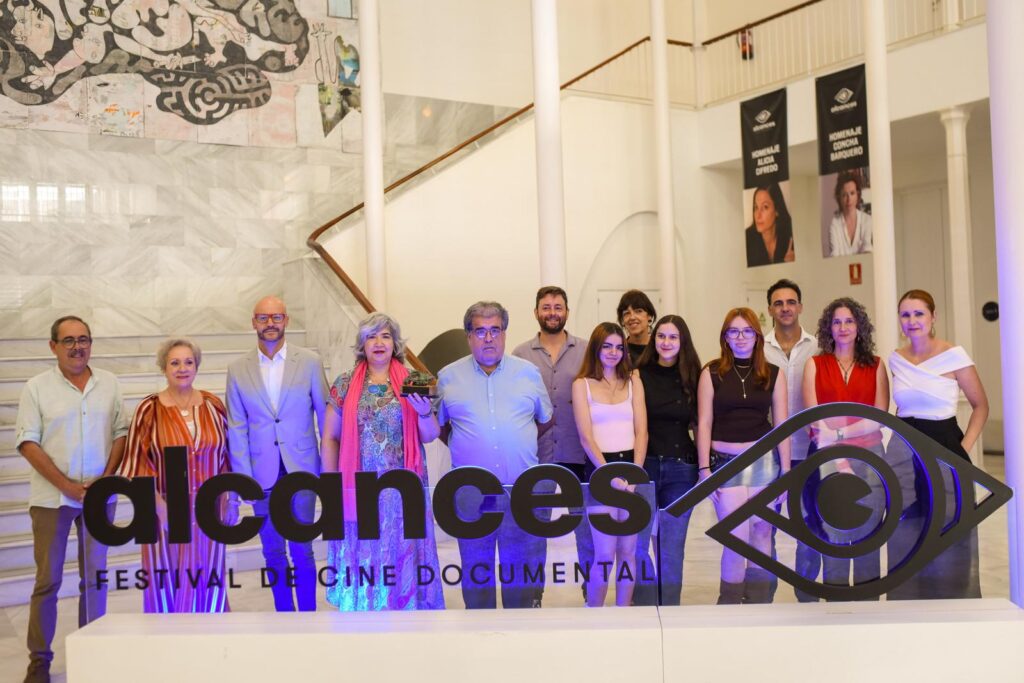 Escenario de una presentación de Alcances con atril negro, micrófono y logotipo del festival al fondo
