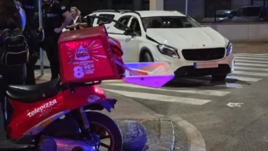Motocicleta roja de reparto y turismo Mercedes blanco junto a un paso de peatones durante la noche.