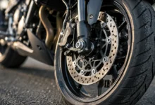 Primer plano de la rueda y el freno de una motocicleta sobre el asfalto, en una composición editorial relacionada con el accidente mortal en Jerez.