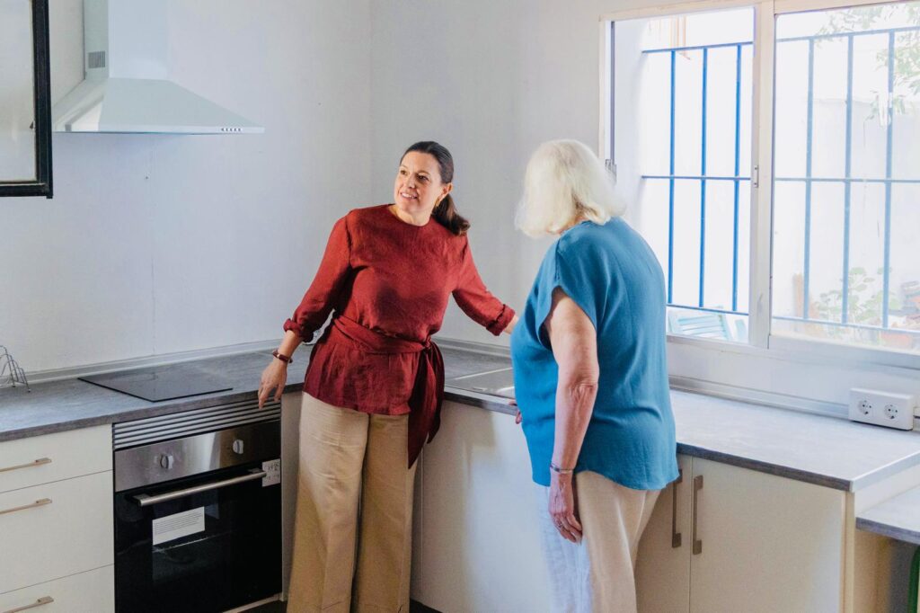 Cuatro personas adultas conversan en un patio interior con pavimento de losas y plantas en macetas.