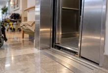 Primer plano de las puertas metálicas de un ascensor y sus guías inferiores en un entorno interior.