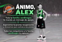 Primer plano de un balón de baloncesto sobre una pista deportiva, con su textura de cuero sintético y una canasta desenfocada al fondo.