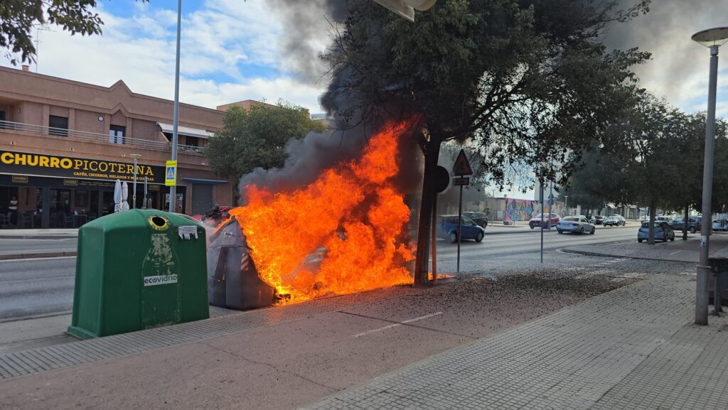 Contenedor de residuos incendiado en una calle urbana durante la tarde