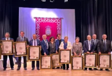 Grupo de doce personas sobre un escenario con cuadros enmarcados y un estandarte rojo al fondo.