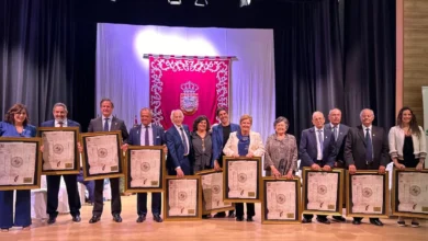 Grupo de doce personas sobre un escenario con cuadros enmarcados y un estandarte rojo al fondo.